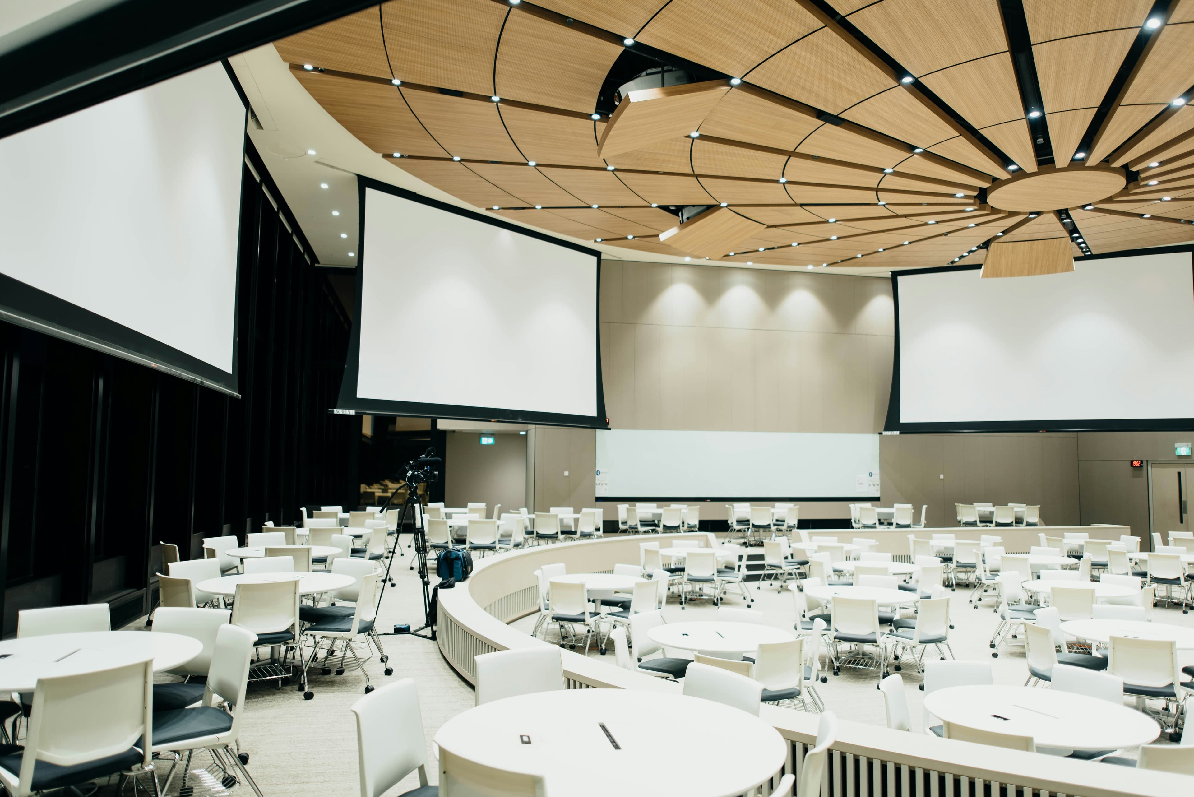 A convention hall laid out with round banquet tables and projection screens